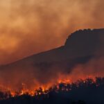 Wildfire burning across a European hillside at dusk